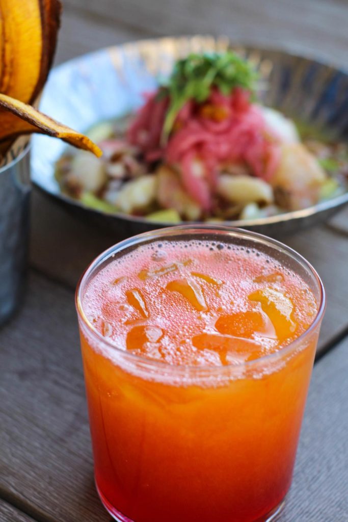 summer cocktail filled with ice next to plated food dish